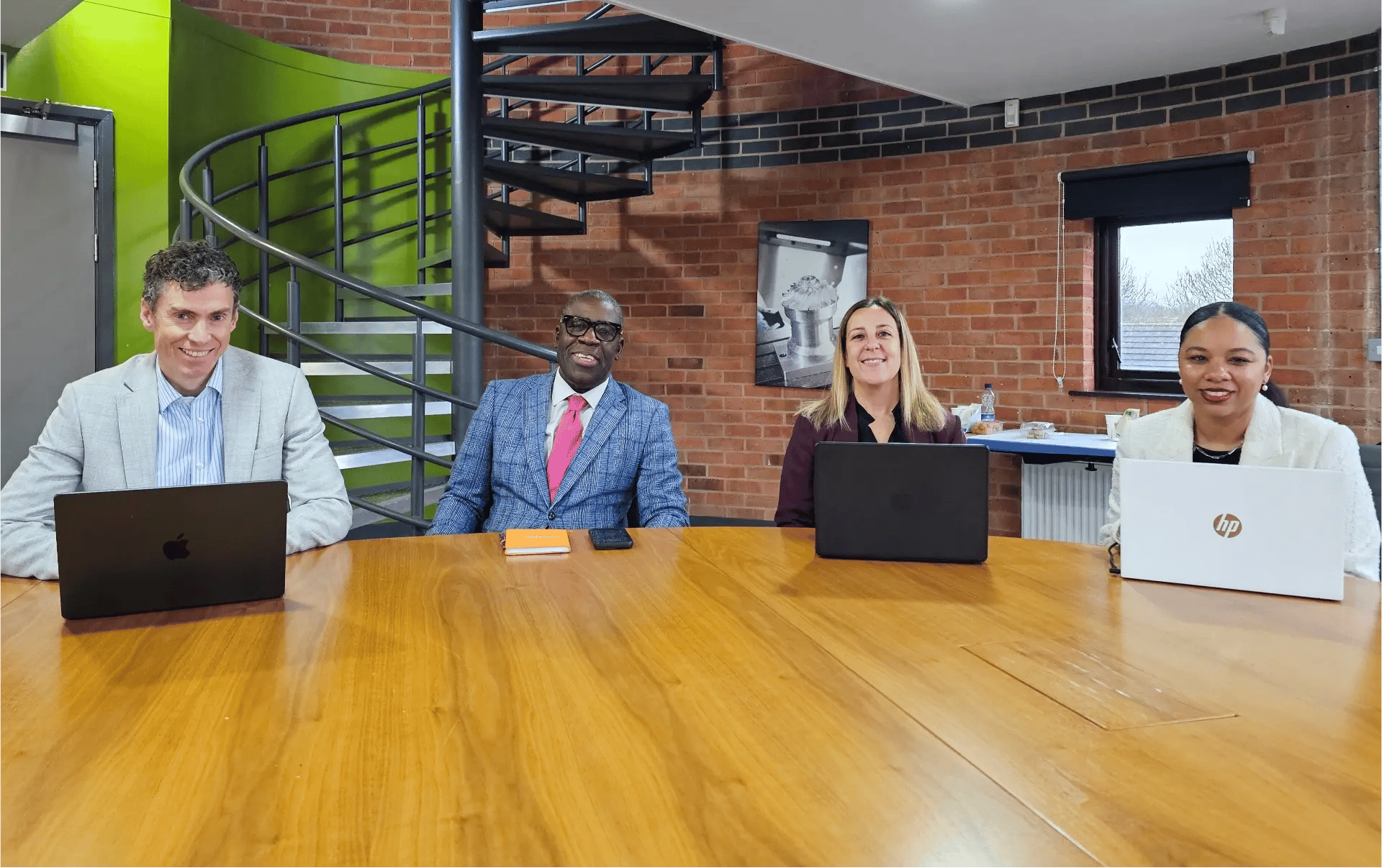JDR Group directors and the social media manager sitting together at a meeting table with laptops, smiling during a strategy discussion.