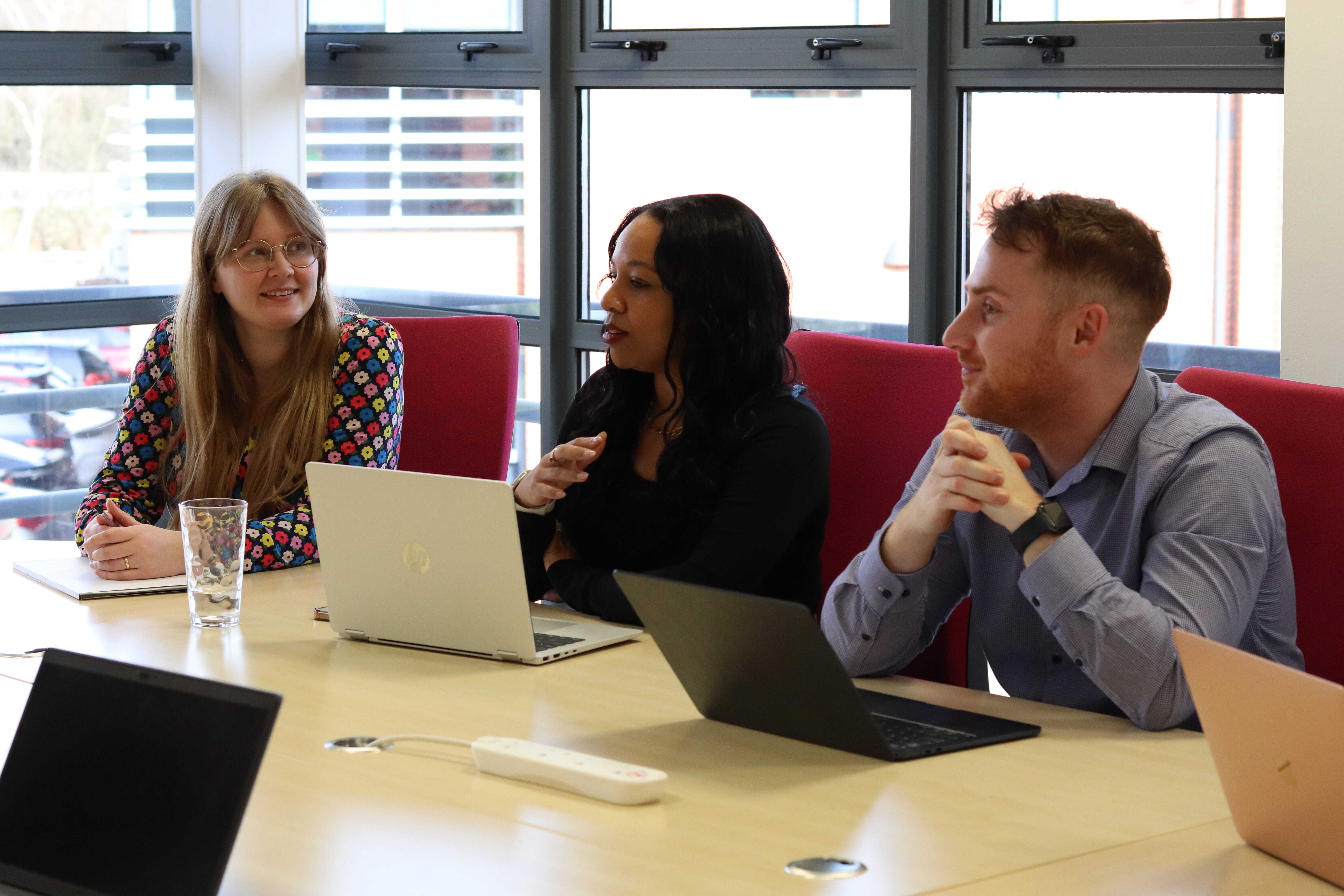 Emma, Kerry, and John in a meeting with their laptops and notebooks discussing the buyer's journey.