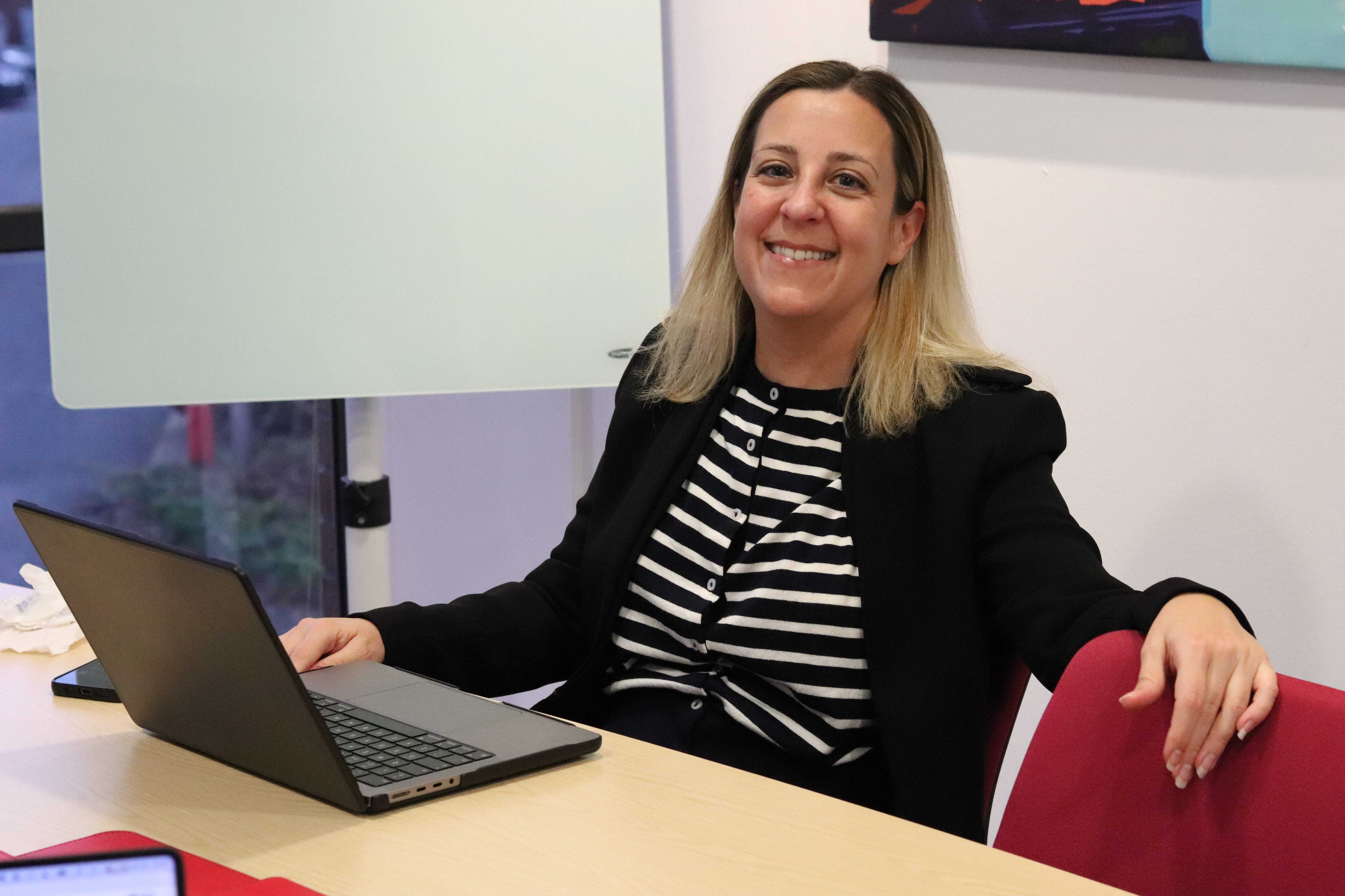 Leanne, one of the directors of JDR group, sitting in front of a laptop at a desk and smiling.