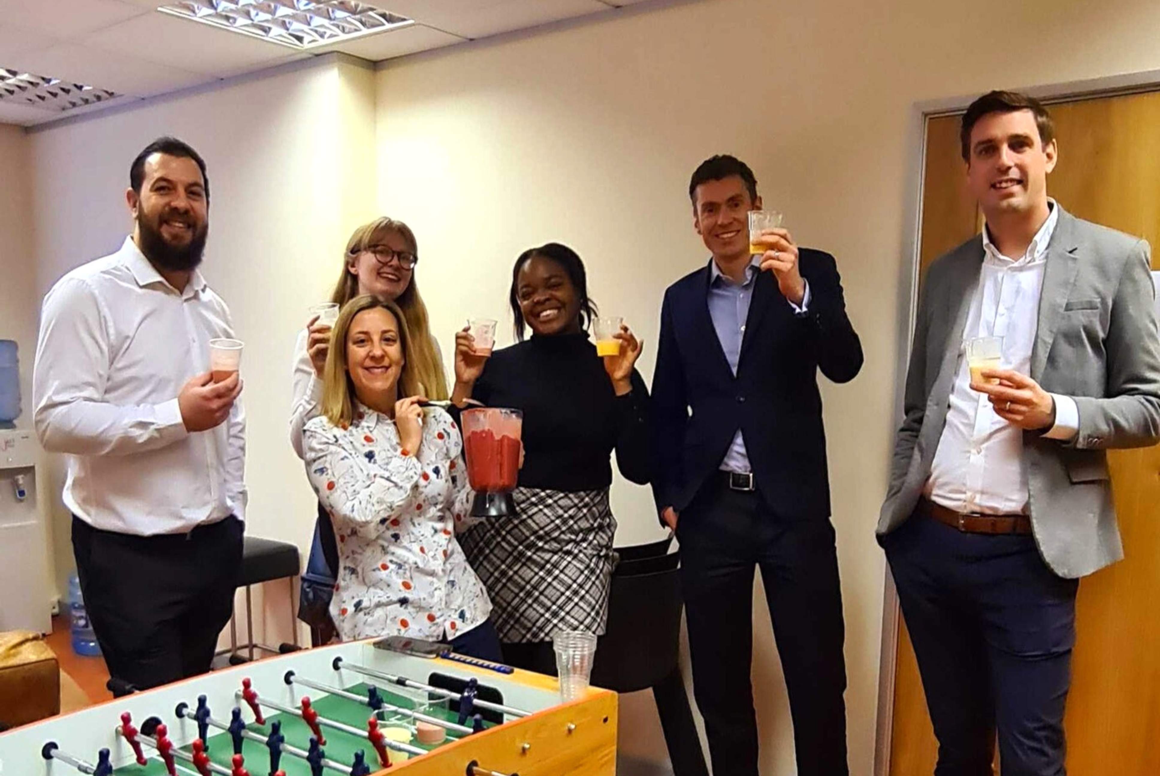 A group of the JDR team in the office canteen drinking pink smoothies for National Nutrition Day