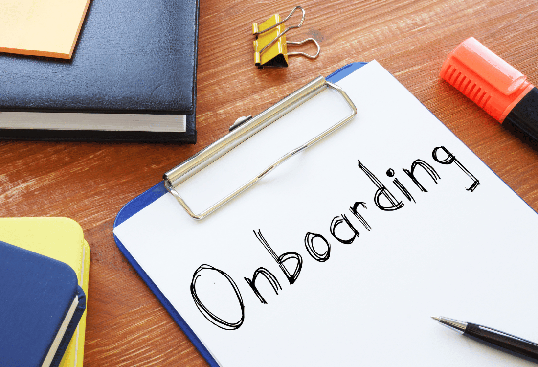 Onboarding written on a piece of paper on a wooden desk with a notebook.