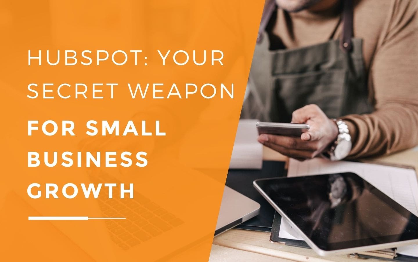 A small business owner in an apron sitting at his desk using HubSpot on his laptop, while making sales on his phone with his iPad on a pile of files.