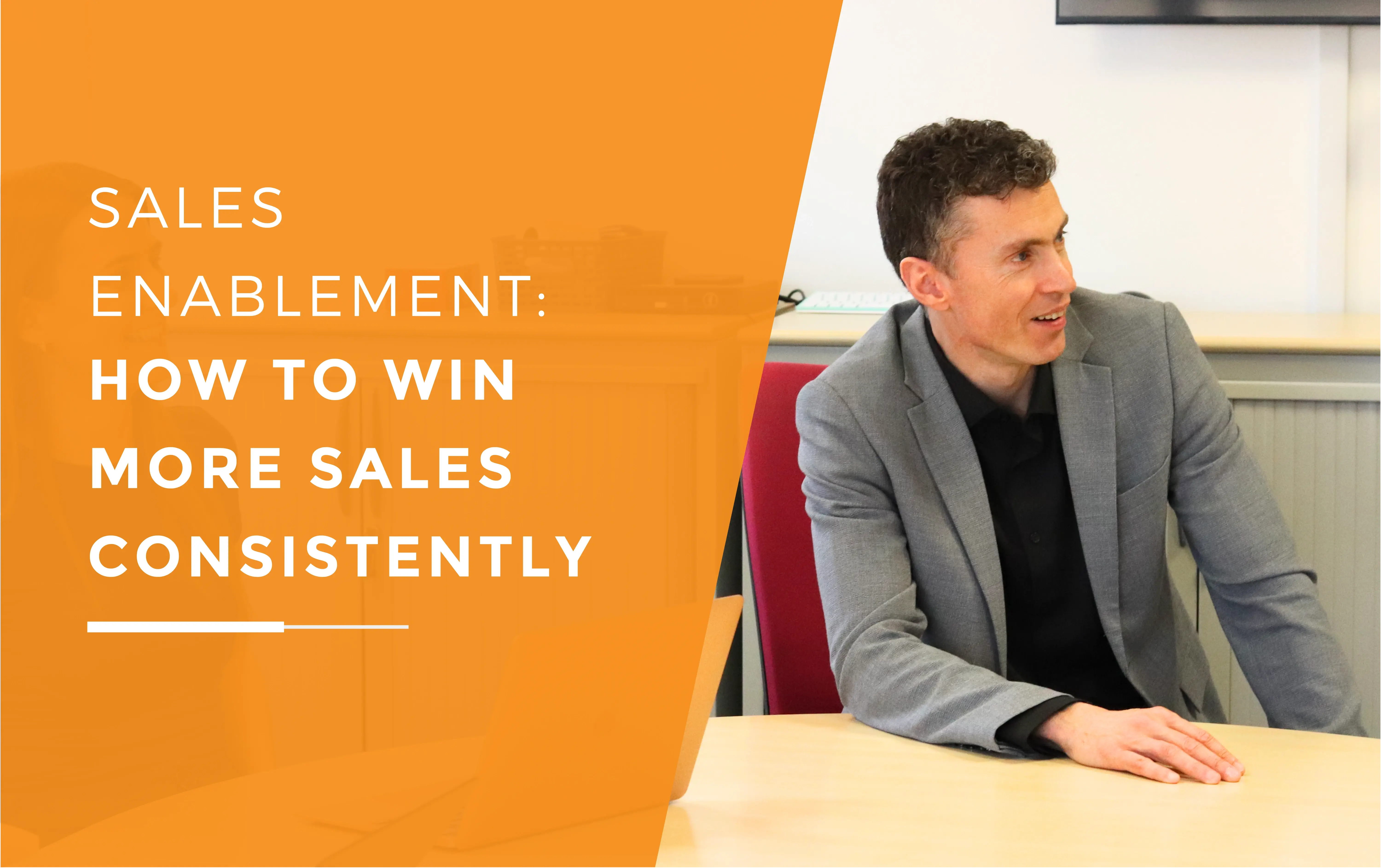 Will wearing a suit with his hand resting on the table during a meeting about sales enablement.